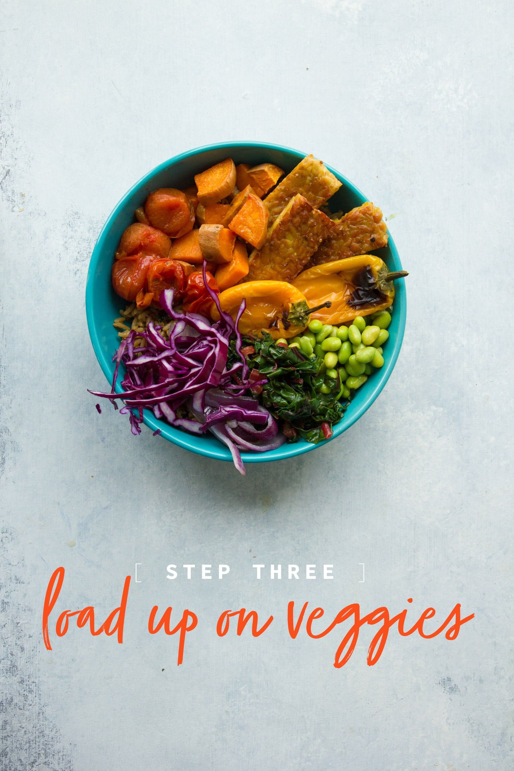 A grain bowl piled high with veggies, tofu, and more veggies. A text overlay reads "Step 3: load up on veggies."