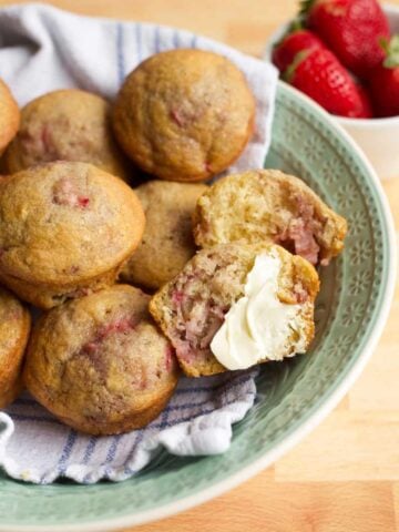 A bowl of strawberry muffins. One muffin is cut in half and smeared with butter.