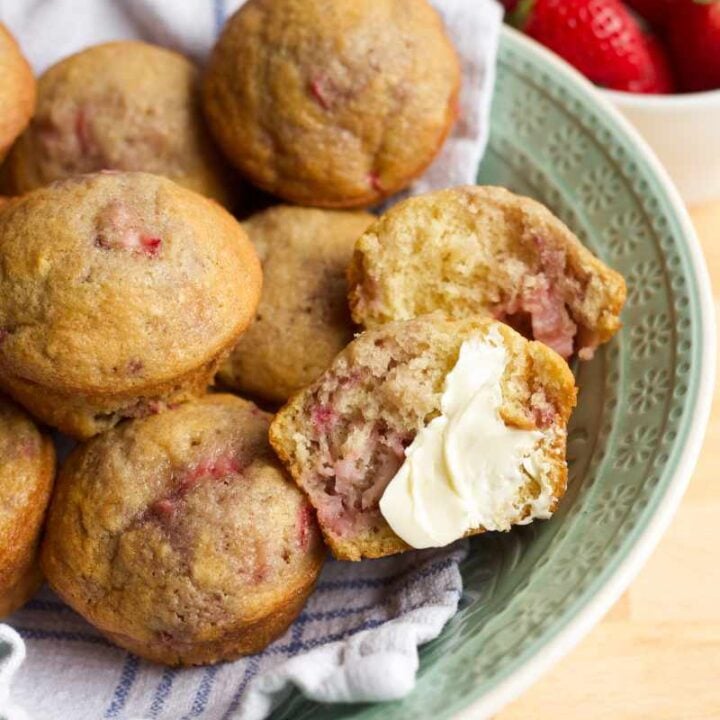 A bowl of strawberry muffins. One muffin is cut in half and smeared with butter.