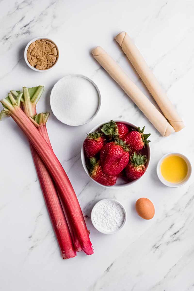 Overhead of ingredients needed to make strawberry rhubarb pie including two pie crusts, stalks of rhubarb, and strawberries.