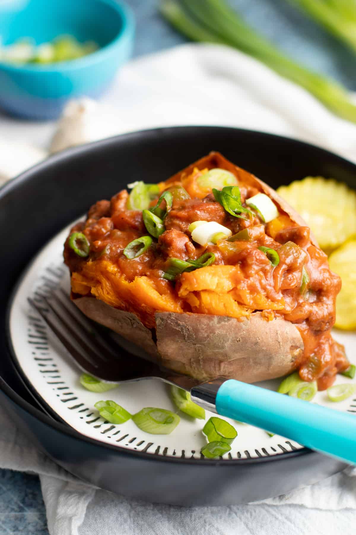 Sweet potato stuffed with a beef sauce on a plate, with a teal-handled fork resting on the side of the plate.