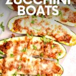 Close view of stuffed zucchini on a long white serving platter garnished with chopped fresh basil. A text overlay reads, "Stuffed Zucchini Boats."