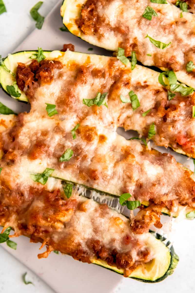 Tight view of cheesy stuffed zucchini plated and garnished with chopped fresh basil.