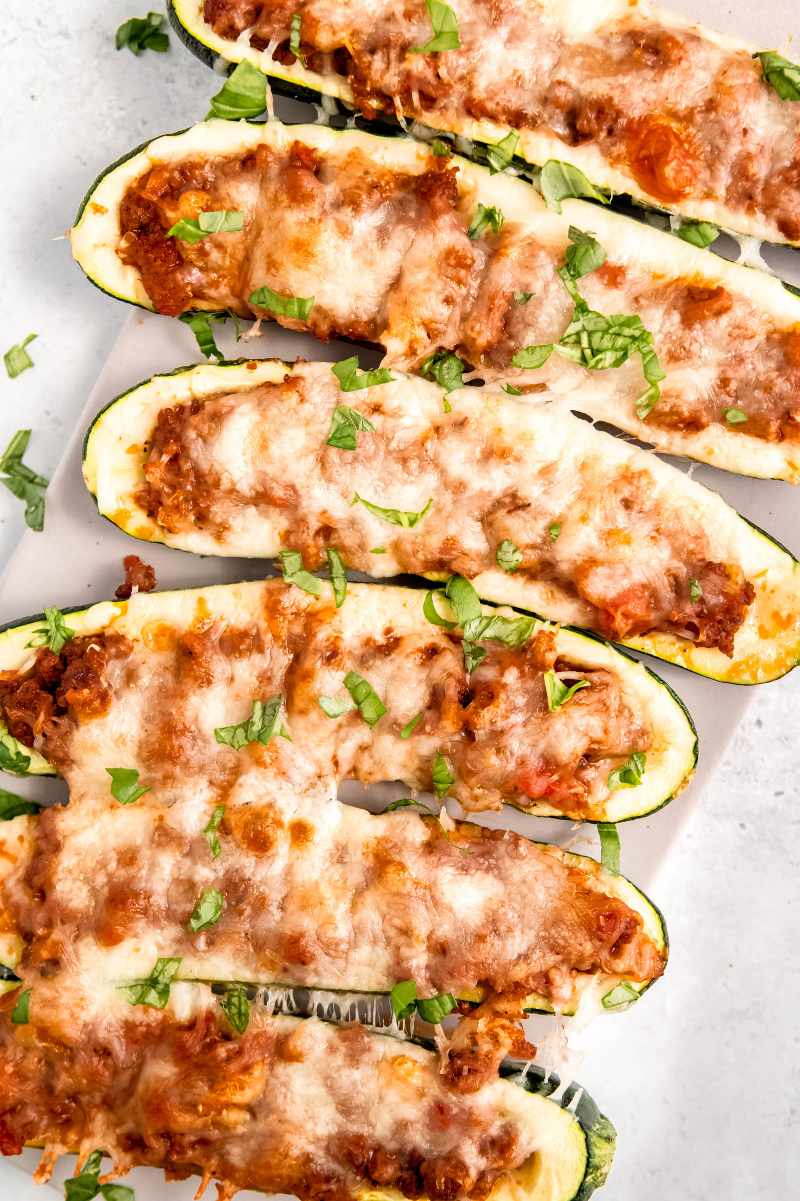 Close view of stuffed zucchini on a long white serving platter garnished with chopped fresh basil.