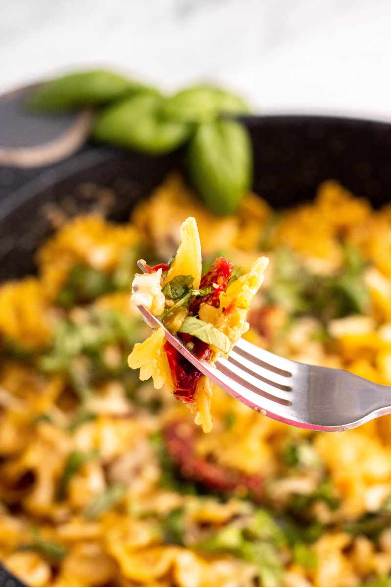 Tight view of a bite of creamy bowtie pasta and sun-dried tomatoes on a fork.