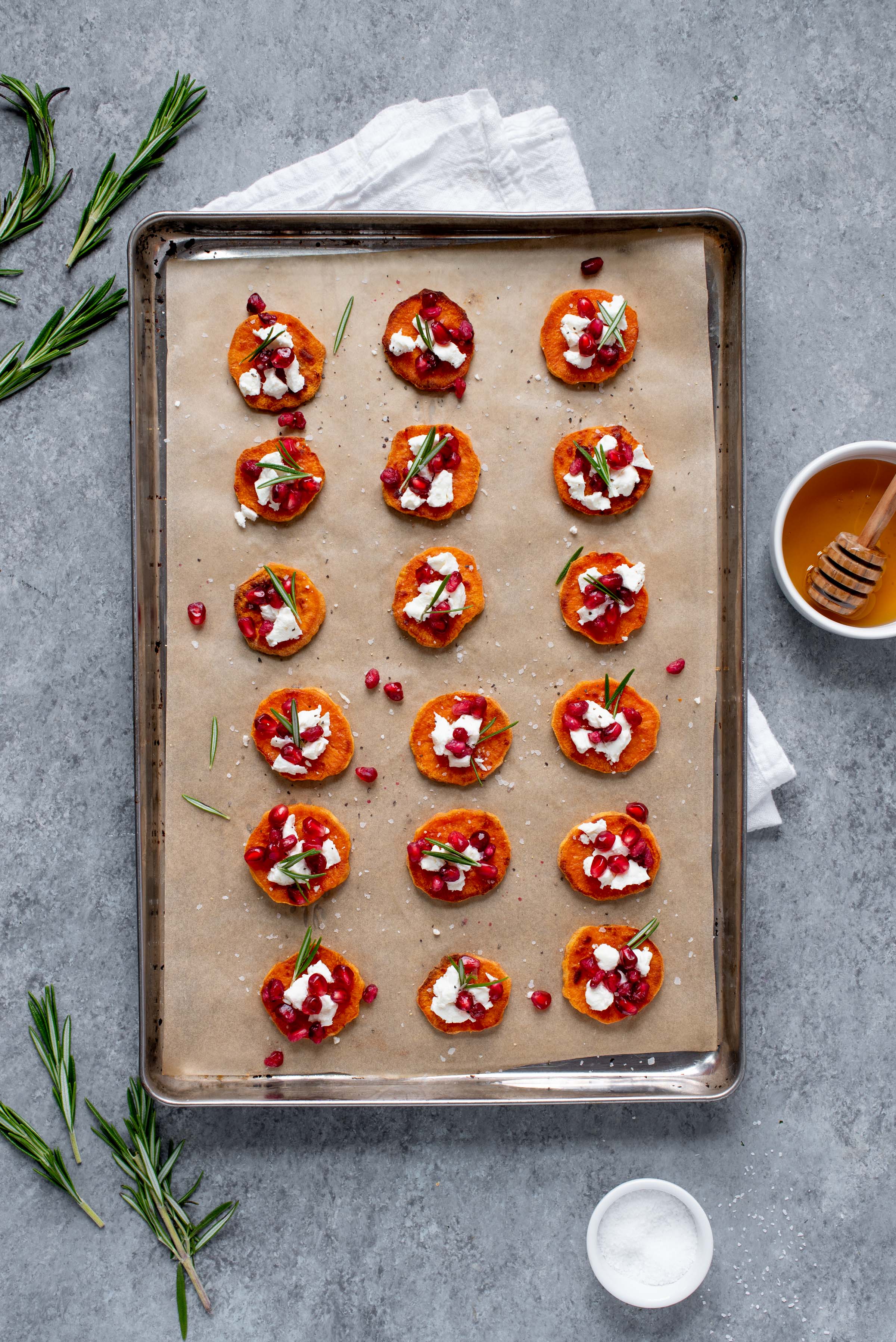 Sweet Potato Crostini with Goat Cheese and Pomegranate spread out on a baking sheet lined with parchment paper