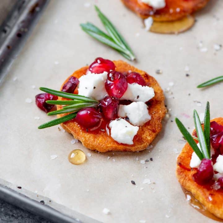 Assembled Sweet Potato Crostini with Goat Cheese and Pomegranate on a baking sheet lined with parchment paper