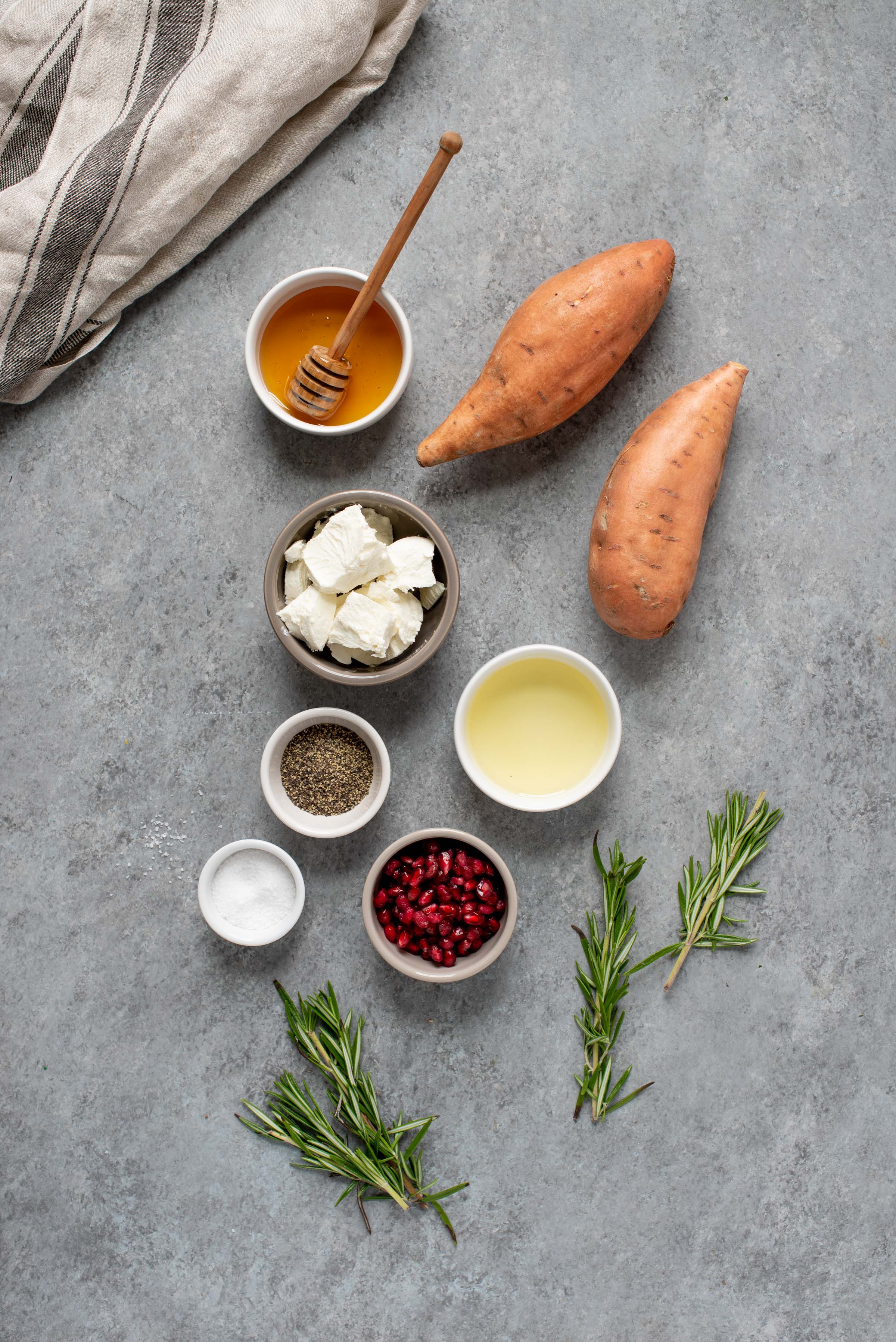 Ingredients for Sweet Potato Crostini with Goat Cheese and Pomegranate on a grey background - sweet potatoes, goat cheese, honey, pomegranate arils, fresh rosemary, and seasonings