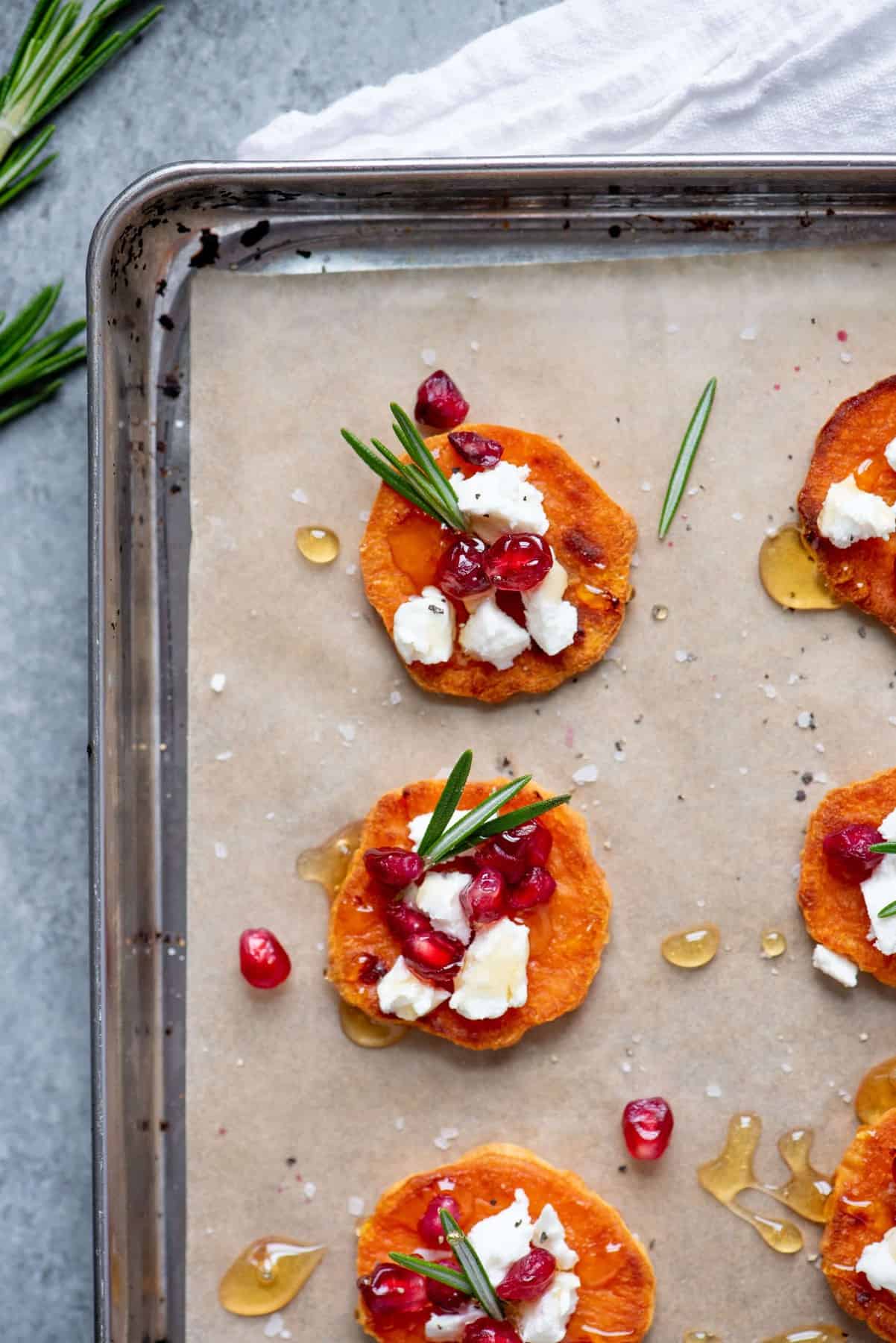 Close up of Sweet Potato Crostini with Goat Cheese and Pomegranate spread out on a baking sheet lined with parchment paper