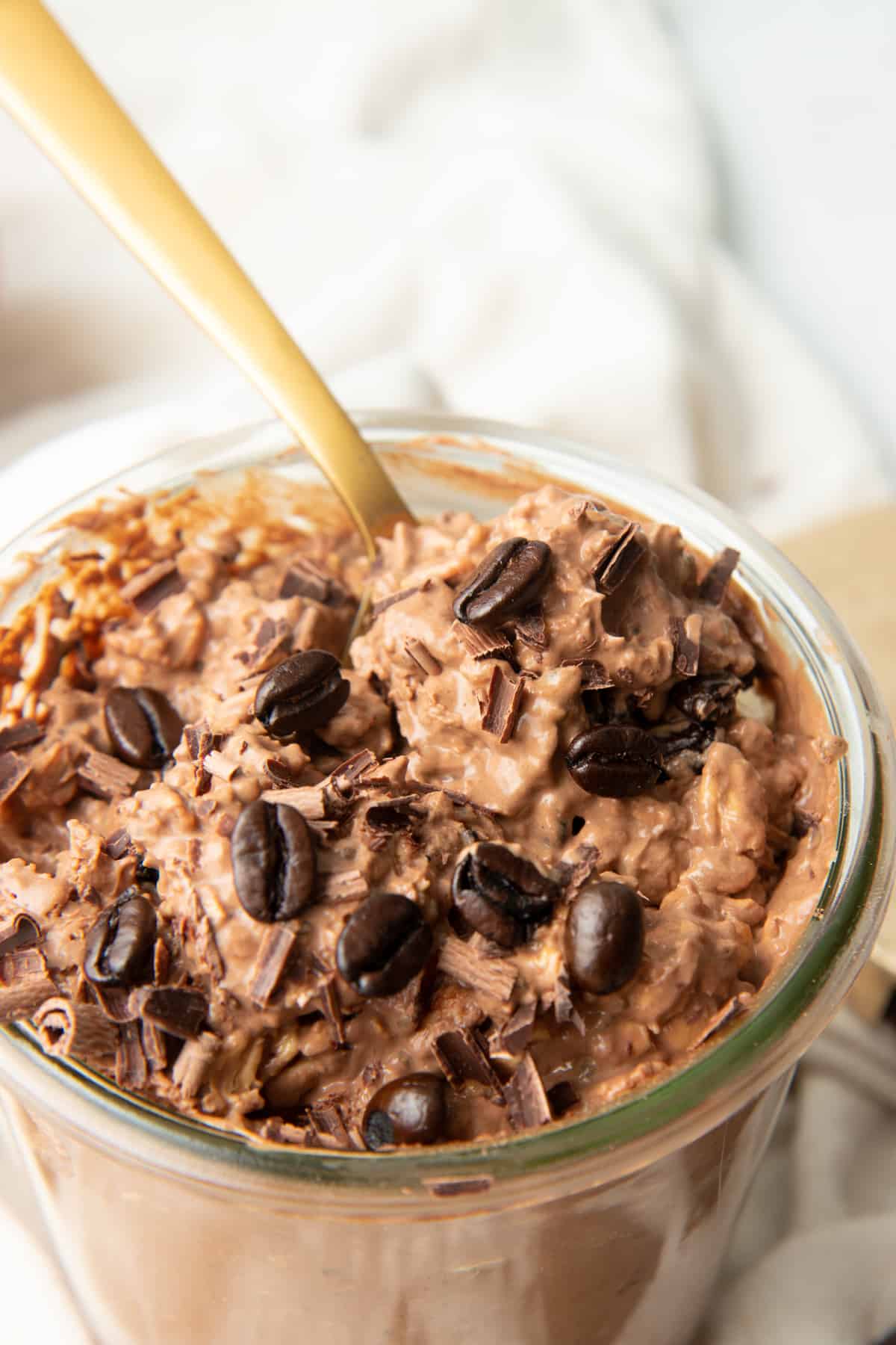 A spoon rests in a jar of chocolate coffee overnight oats.