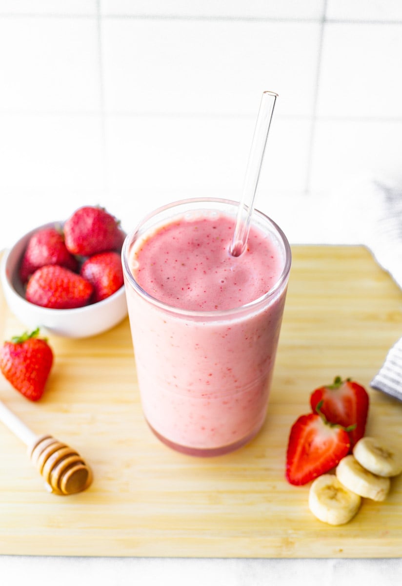 Overhead of finished smoothie on a cutting board with fresh strawberries and banana slices.