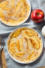 Two thin pancakes served on white plates with an apple and forks nearby.