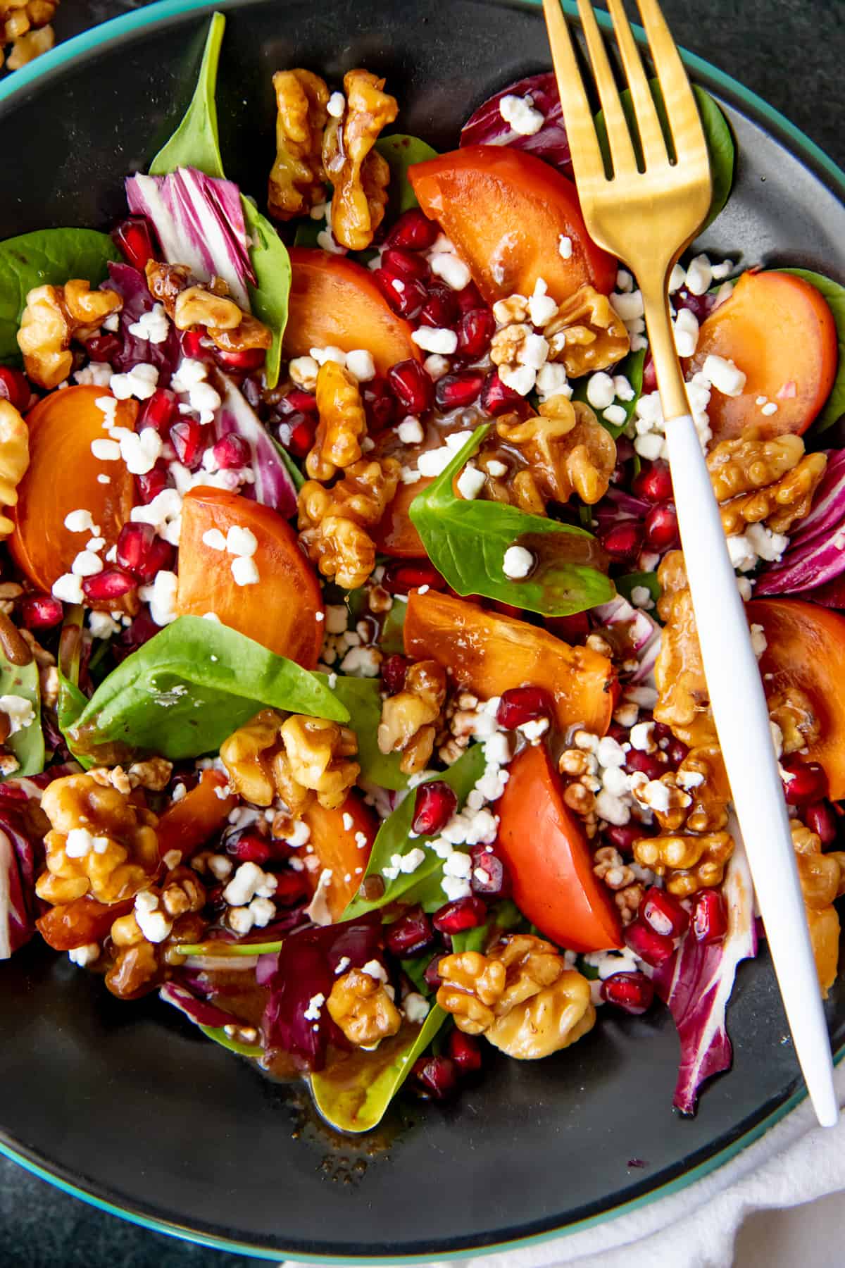 Close up of a salad filled with pomegranates, persimmons, spinach, candied walnuts, and goat cheese.