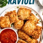 Overhead of toasted ravioli served on a white plate with a small bowl of marinara sauce. A text overlay reads, "Toasted Ravioli."