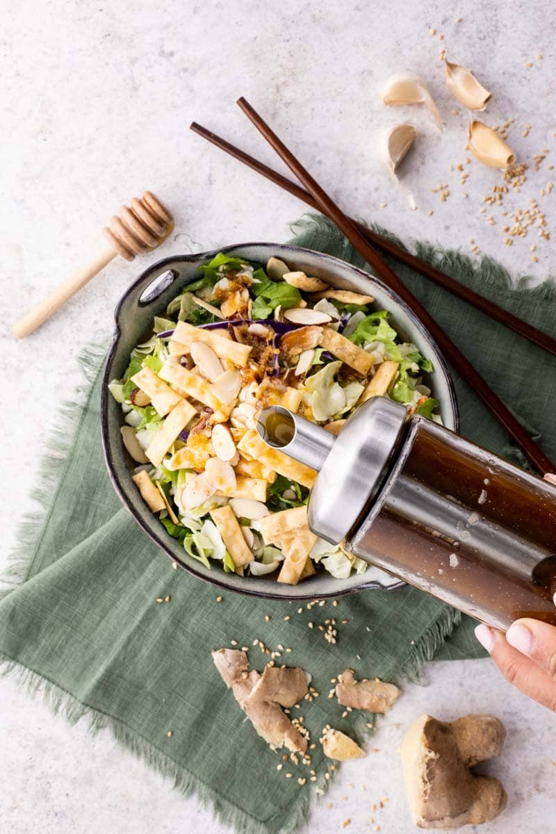 Top view of pouring dressing onto an asian-inspired salad.