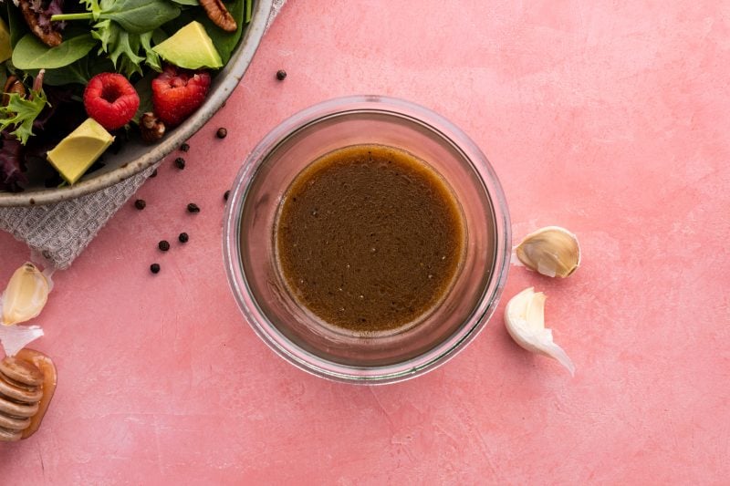 Birdseye view of homemade balsamic dressing in a glass jar alongside a fresh salad.