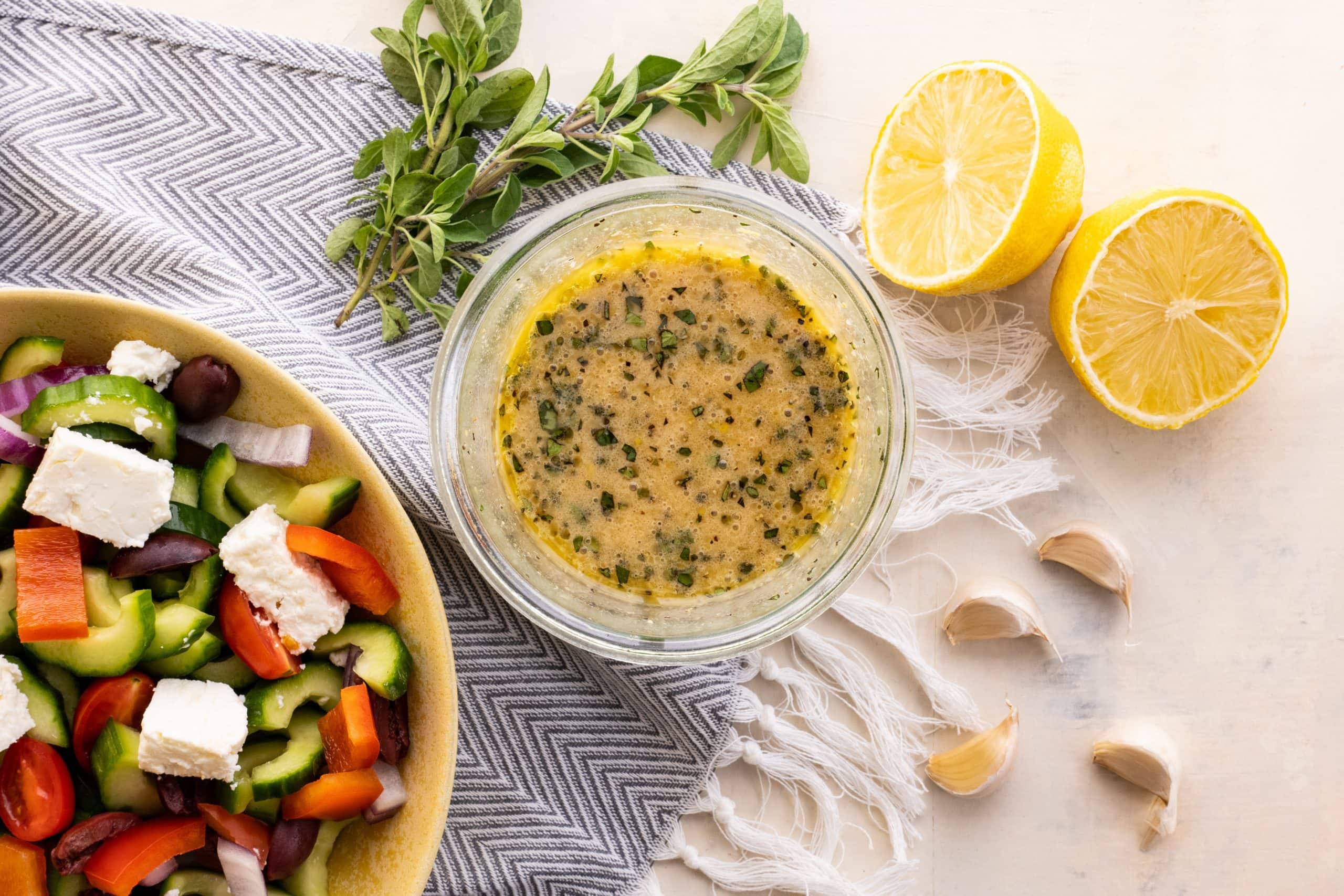 Birdseye view of a glass jar filled with an emulsified vinaigrette alongside a fresh greek salad.