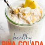 A glass jar filled with tropical coconut overnight oats sits on a marble countertop. The oats are garnished with pineapple and coconut, and a spoon dips into the jar. A text overlay reads "Healthy Piña Colada Overnight Oats."