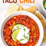 Overhead of a full bowl of finished turkey chili with spoon and linen napkin alongside. A text overlay reads, "Turkey Taco Chili."