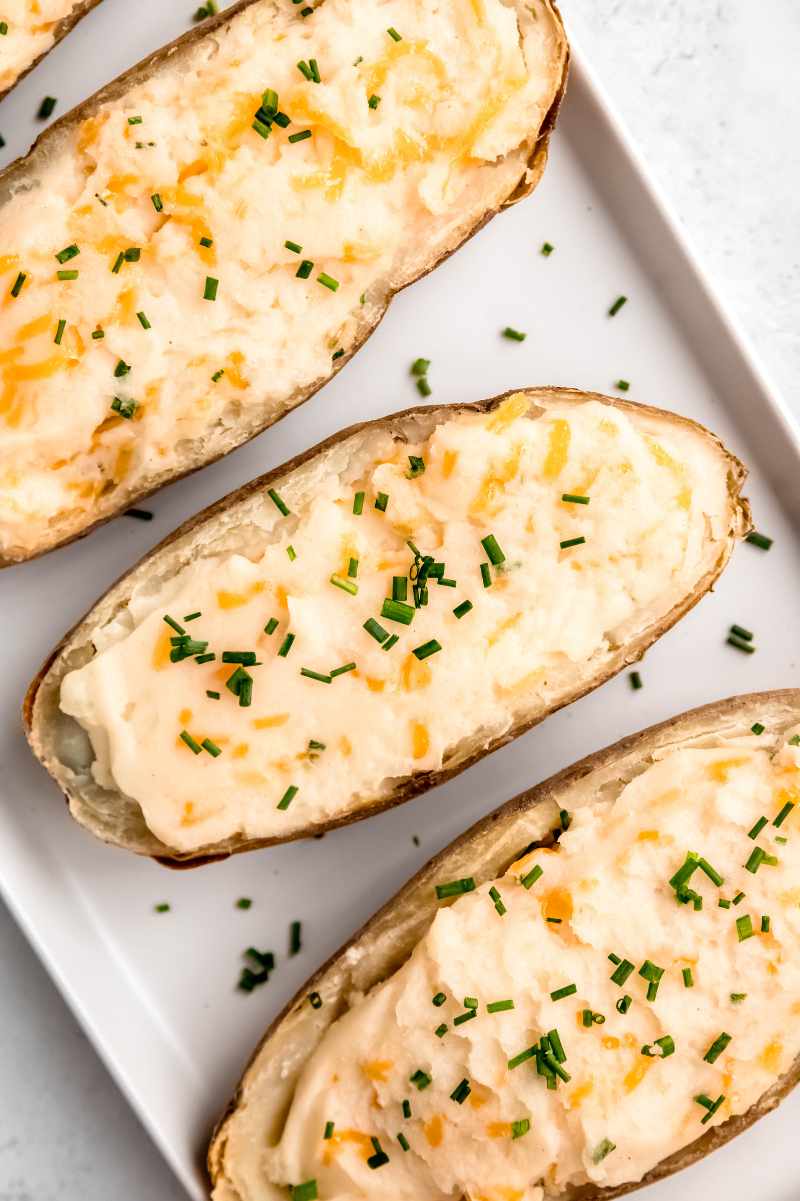 Overhead of three potatoes topped with fresh chives on a long, white, rectangular platter.