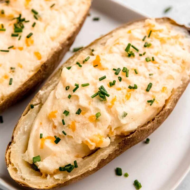 Twice baked potatoes served on a white platter topped with snipped chives.