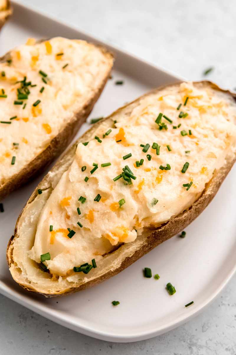 Twice baked potatoes served on a white platter topped with snipped chives.