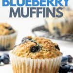 A freshly baked Vegan Blueberry Muffin sits surrounded by fresh blueberries. A text overlay reads, "Vegan Blueberry Muffins".