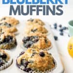 Freshly baked Vegan Blueberry Muffins sit in a muffin pan. A text overlay reads, "Vegan Blueberry Muffins".