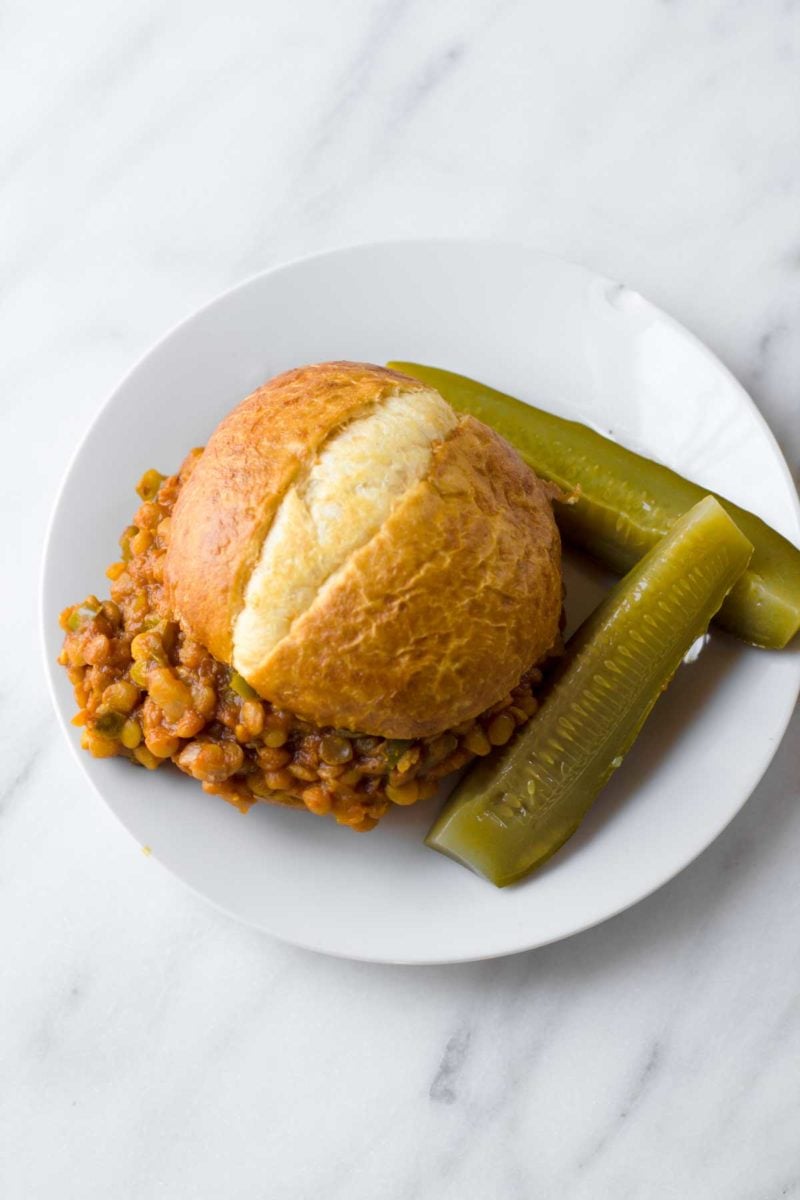 A Lentil Sloppy Joe sits on a white plate, with pickles off to the side