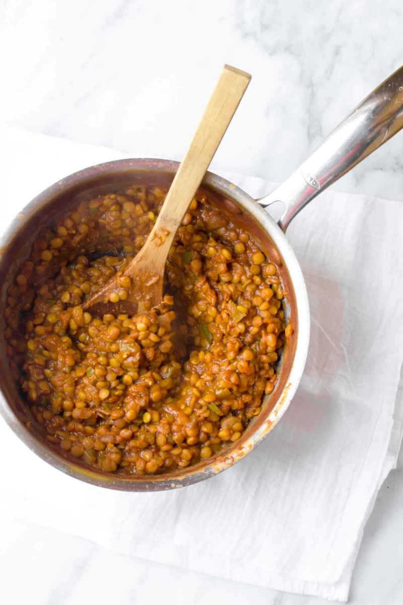 A bowl of sloppy joe mixture sits in a sauce pan. A wooden spoon is inside the pot.