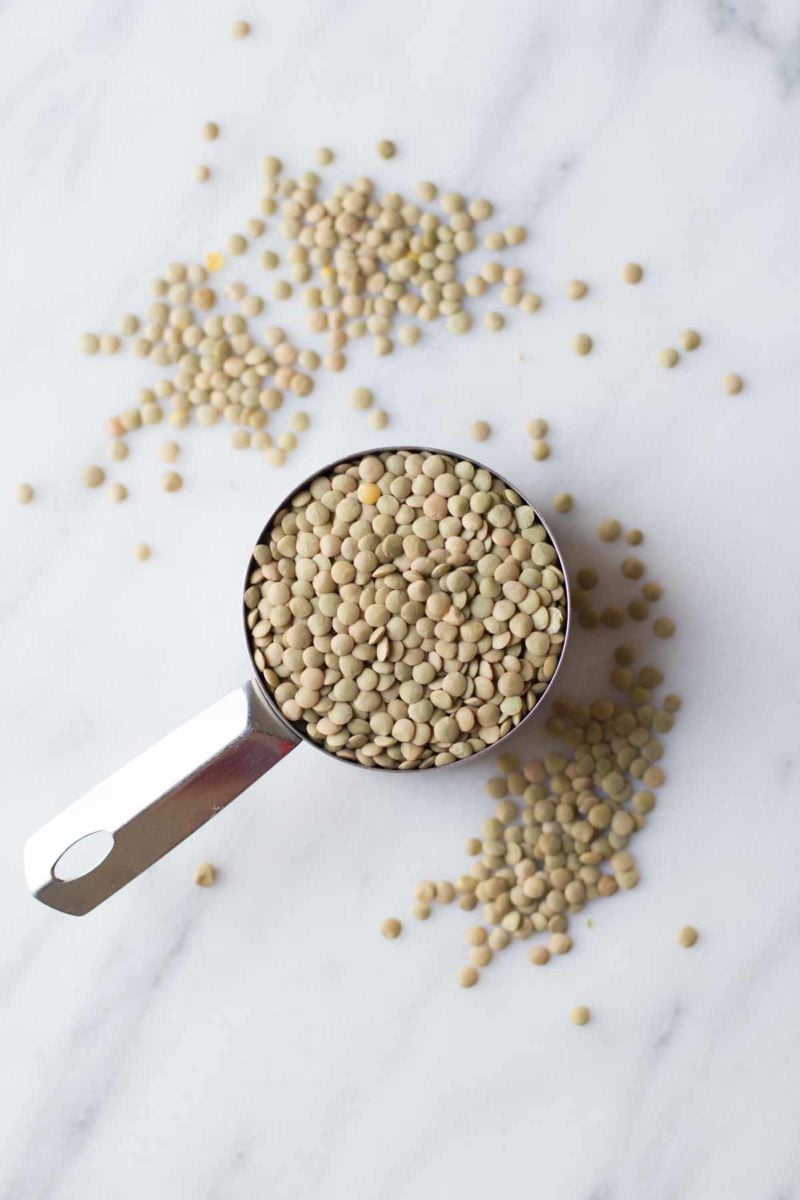 Raw lentils sit in a measuring cup, on a white background.