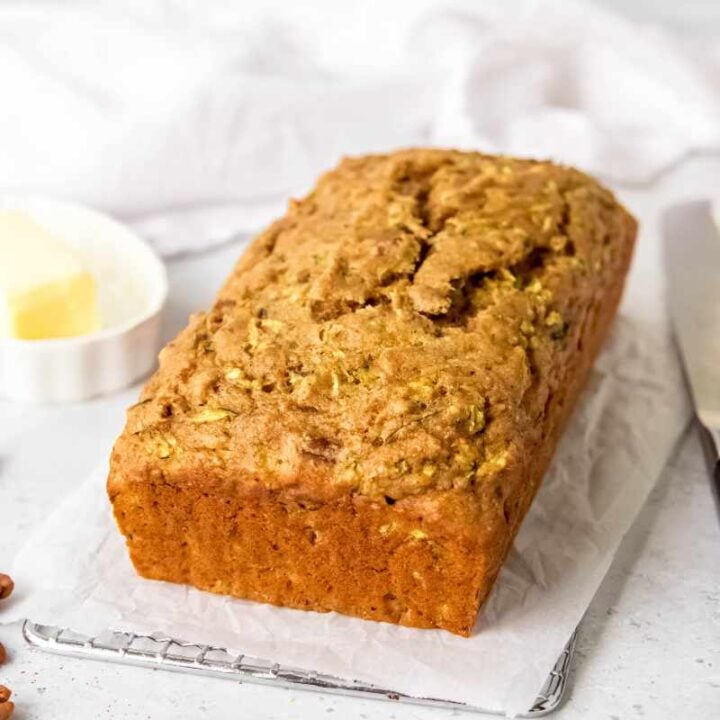 A whole loaf of zucchini bread cooling on a parchment paper lined metal cooling rack.