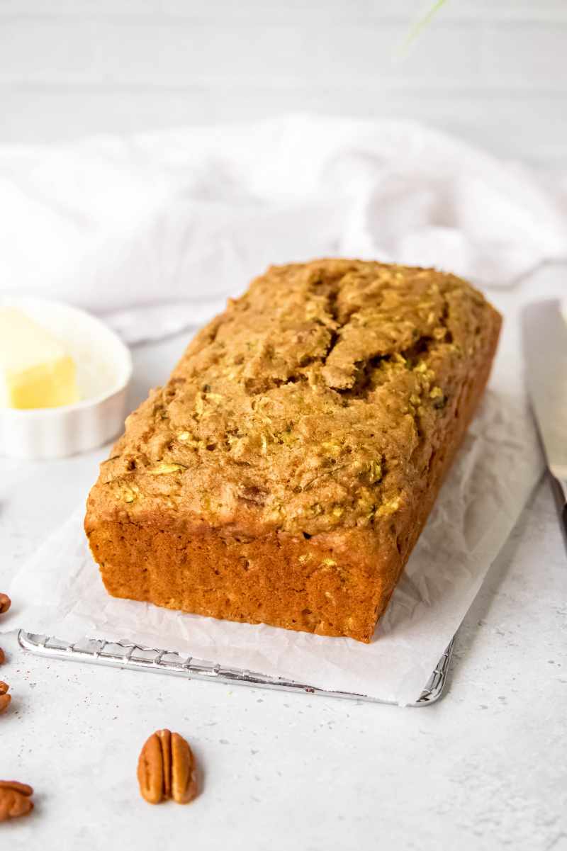 A whole loaf of zucchini bread cooling on a parchment paper lined metal cooling rack.