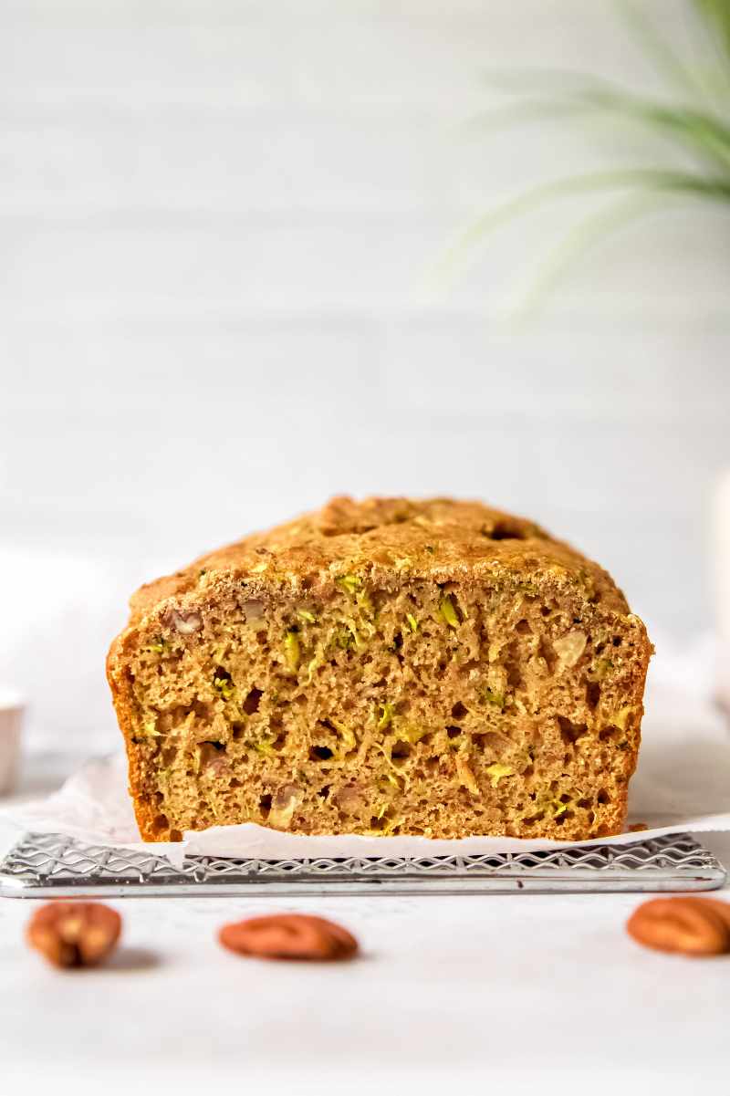 A cut loaf of zucchini bread showing the shreds of zucchini and pecan pieces sprinkled throughout.