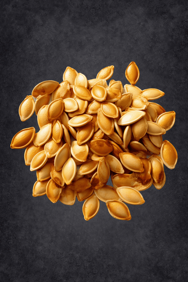 A pile of roasted pumpkin seeds rests on a black background