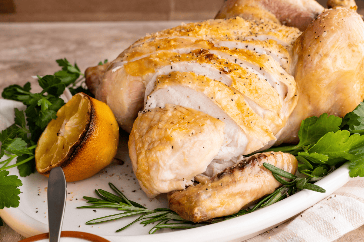 A roast chicken on a white platter, with the breast sliced