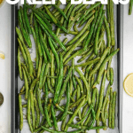 Overhead of a parchment paper lined sheet pan with roasted green beans on a white table. A text overlay reads, "Oven-Roasted Green Beans."